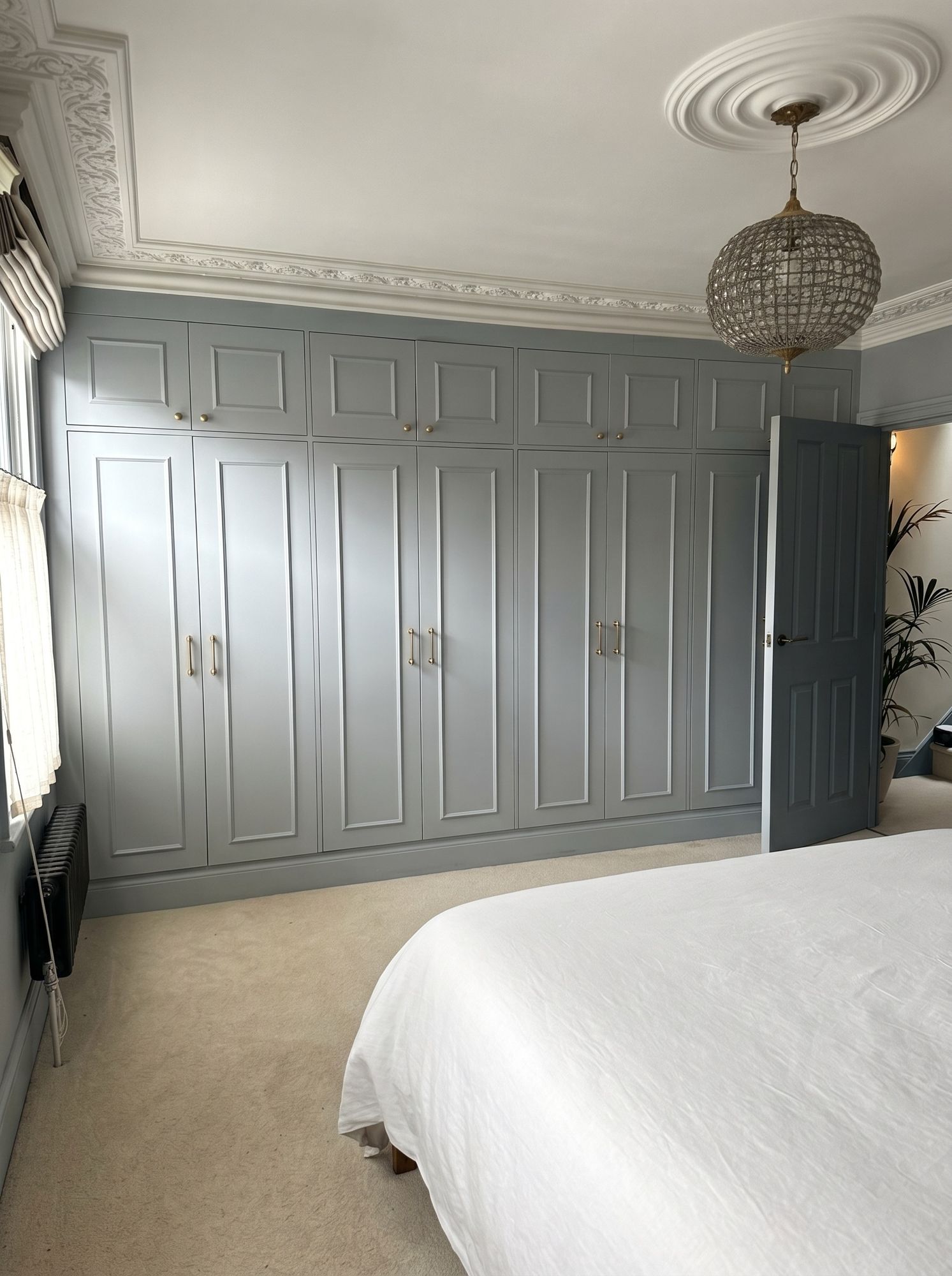 Wall of panelled fitted wardrobes in blue-grey with brass handles