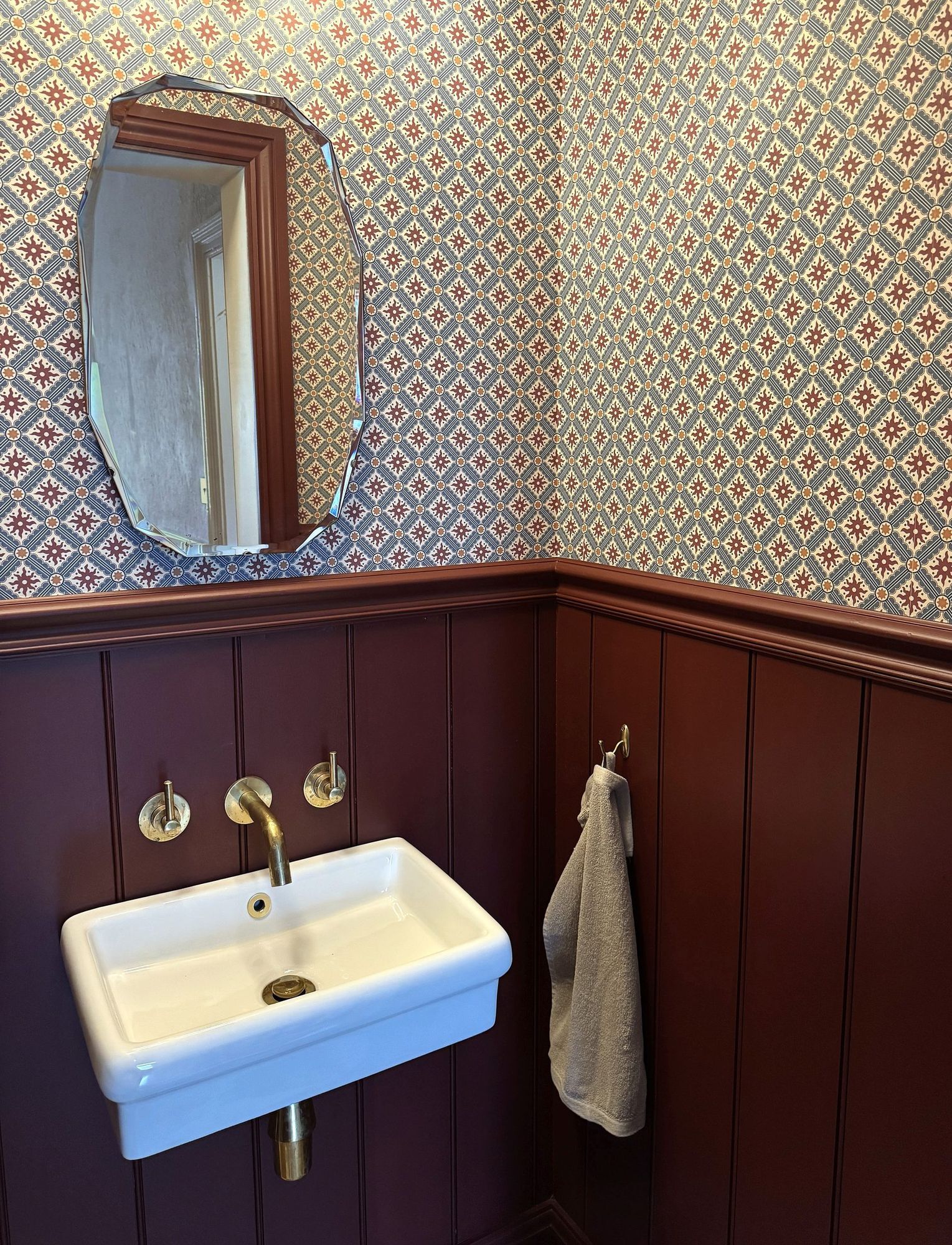 Cloakroom basin with patterned wallpaper and burgundy panelling